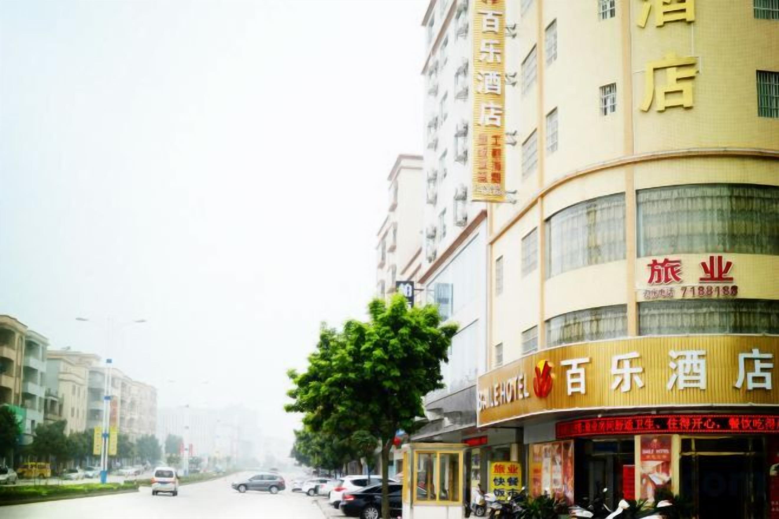 A hotel with a signboard, a visible entrance, and a street view with parked cars.