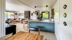Amplia sala de estar con una mesa de comedor de madera, un sofá y una cocina con armarios azules y pared de ladrillo.