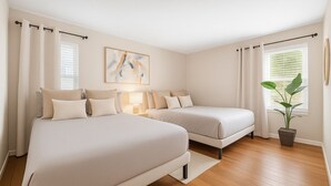 Ein Schlafzimmer mit zwei Betten, einem Nachttisch mit Lampe, einem Bild an der Wand und einer Topfpflanze.