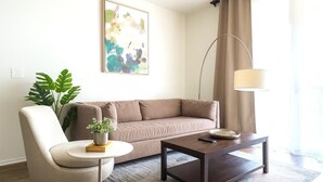 Ein modernes Wohnzimmer mit einem beigefarbenen Sofa, einem runden Couchtisch, einer Stehlampe und einer Zimmerpflanze.