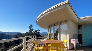 A balcony with a wooden table and yellow chairs, overlooking a mountainous landscape. - Newly renovated penthouse getaway! (Eugene)