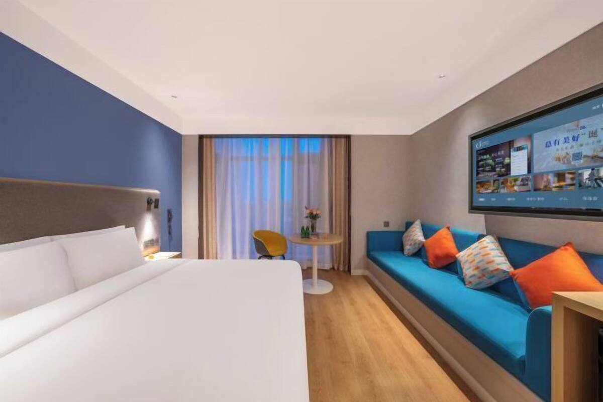 A hotel room with a bed, a sofa, a TV, and a small table with a chair.