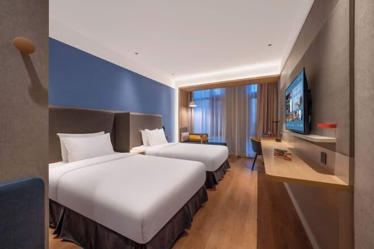 A hotel room with two beds, a desk, a TV, and a window with curtains.