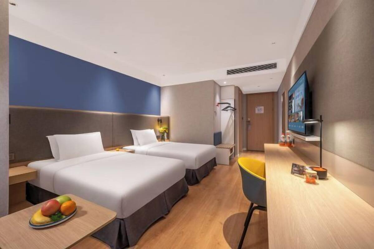 A hotel room with two beds, a desk with a fruit bowl, a TV, and a small seating area.