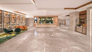 A modern lobby with a marble floor, a reception desk, a bookshelf, and a green sofa. - Orange Hotel (Beijing Daxing Biomedical Base Longhu Tianjie Branch) (Beijing)