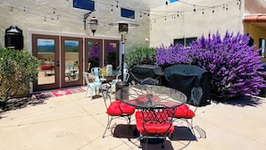 An outdoor patio with a glass table and red cushioned chairs, a barbecue grill, and a purple flowering bush. - Adorable Casita with Pool for 2 People (Tubac)