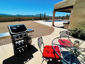 Un patio exterior con una parrilla, zona de estar y vistas a las montañas.