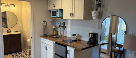 A compact kitchen with white cabinets, a microwave, a coffee maker, and a sink.