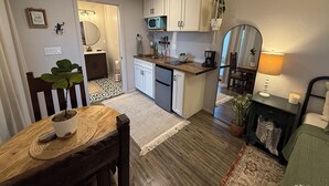 A compact kitchen with white cabinets, a microwave, and a sink. There's a dining area with a wooden table and chairs, and a small rug on the floor. - Adorable Casita with Pool for 2 People (Tubac)