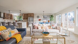 En moderne stue med sofa, sofabord og spiseplads med stole samt et køkken i baggrunden.