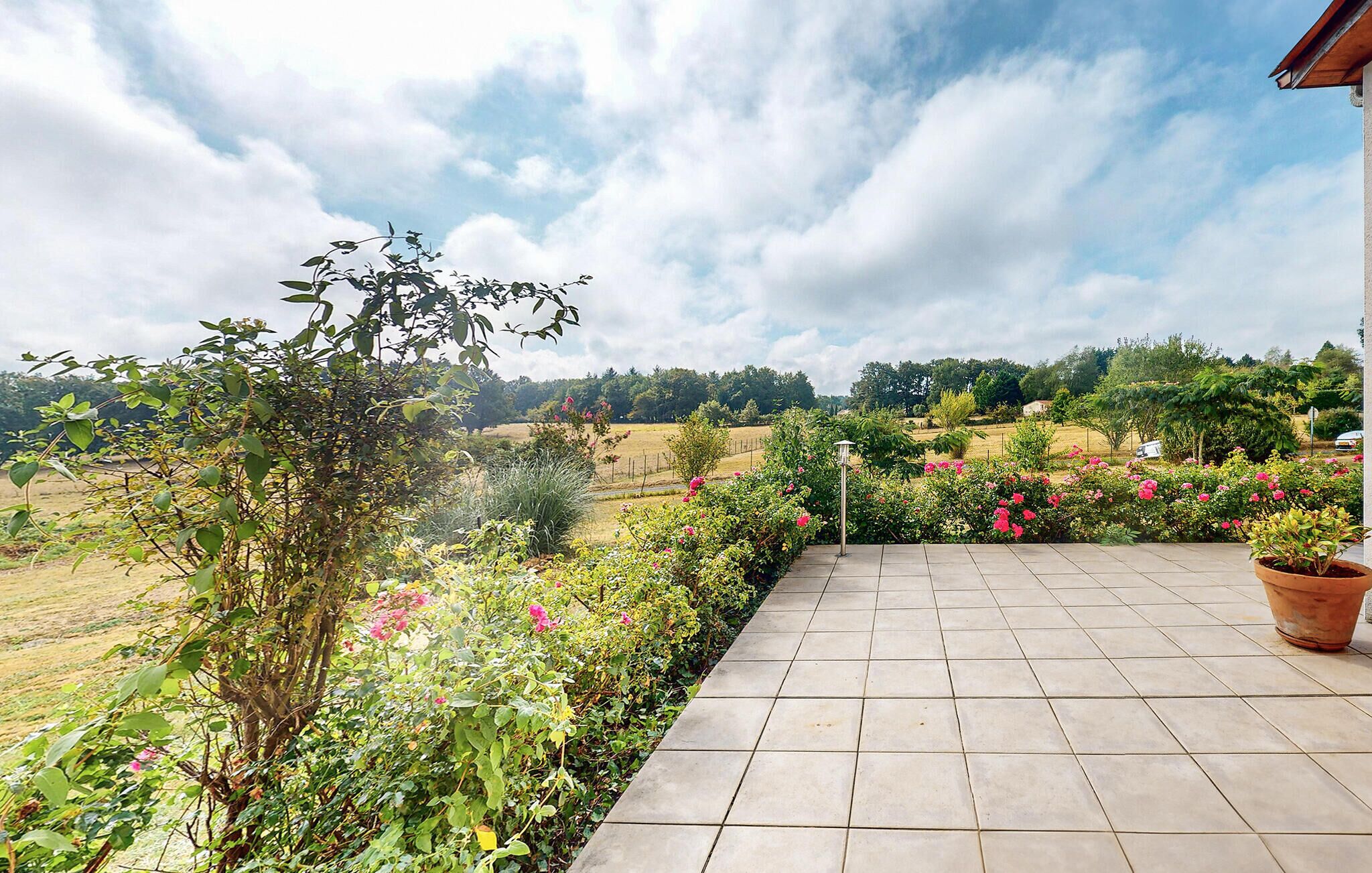 A paved patio with a view of a garden and fields.
