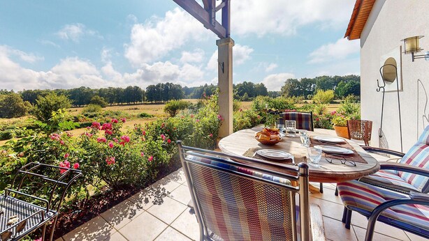 Un patio exterior con una mesa dispuesta para comer, rodeado de sillas, con vistas a un jardín con flores y árboles.