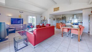 Una sala de estar amplia con un sofá rojo, una mesa de centro de vidrio y un televisor. Hay una zona de cocina con una mesa de comedor y sillas.