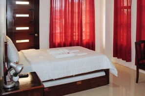 A hotel room with a bed, a bedside table with a lamp, and red curtains. - RedDoorz @ LS Suites Poblacion Culasi Antique (Culasi)