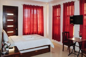 Quarto de hotel com cama, escrivaninha, cadeira e televisão.