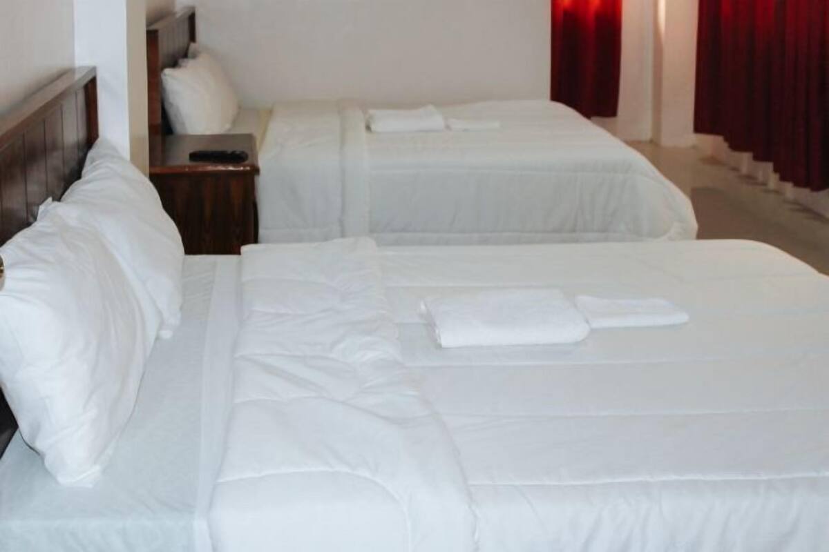 Habitación de hotel con dos camas, una mesita de noche y una cortina roja.