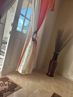 A room with a door leading to an outdoor area, a vase with dried plants, and a patterned rug on the floor. - StayHaven Escapes (Saint Thomas)