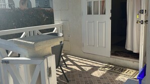 Een zonnig terras met een witte deur, een kleine tafel en een stoel.