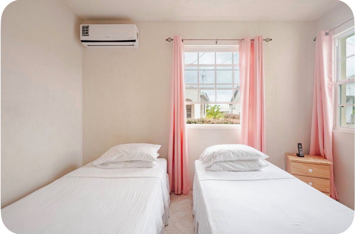 A hotel room with two single beds, a bedside table with a phone, and an air conditioning unit.