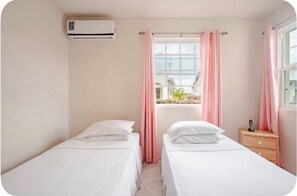 A hotel room with two single beds, a bedside table with a phone, and an air conditioning unit.