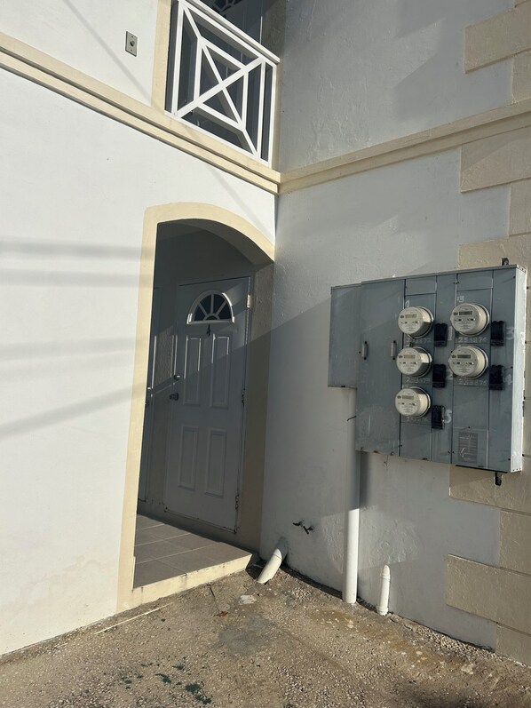 A building with a white facade, a grey utility box with meters, and a white door with an arched top.