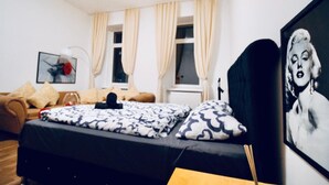 Een slaapkamer met een bed, een bank, een raam met gordijnen en een lijst met een afbeelding aan de muur.