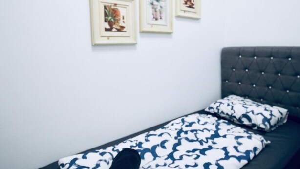 Een eenpersoonsbed met een gestoffeerd hoofdbord, een bed met een patroon en drie ingelijste foto’s aan de muur.
