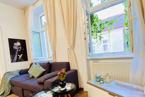 Un salon avec un canapé, une petite table sur laquelle est posé un vase, une fenêtre avec des rideaux et un radiateur.