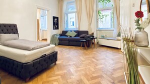 Una habitación con cama, sofá, una mesita y ventana con cortinas.