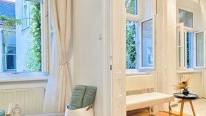Una habitación con un banco, una mesa pequeña con un florero y una ventana con cortinas.