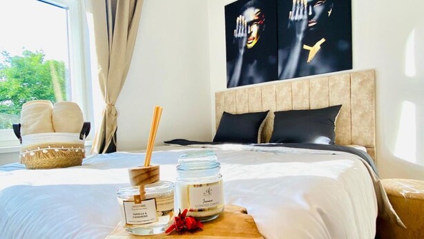 Una cama bien hecha con una bandeja de madera que contiene dos velas perfumadas, un cojín decorativo y una cesta trenzada.