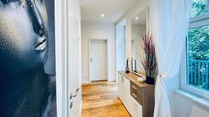 Un pasillo moderno con suelo de madera, una puerta blanca, un espejo y una ventana con vistas a zonas verdes.