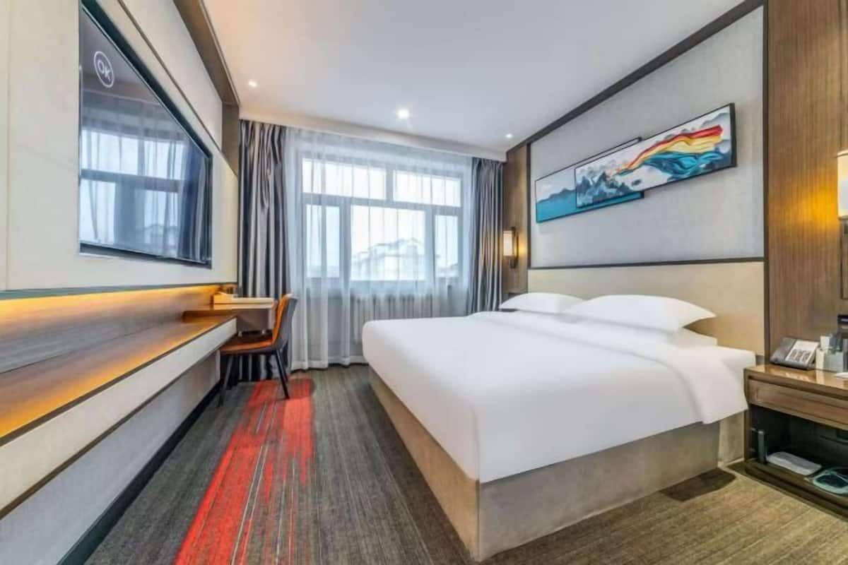 Een hotelkamer met een bed, een bureau, een stoel, een televisie en een schilderij aan de muur.