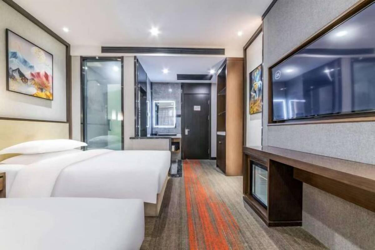 Een hotelkamer met twee bedden, een televisie, een badkamer en een gang naar een andere kamer.