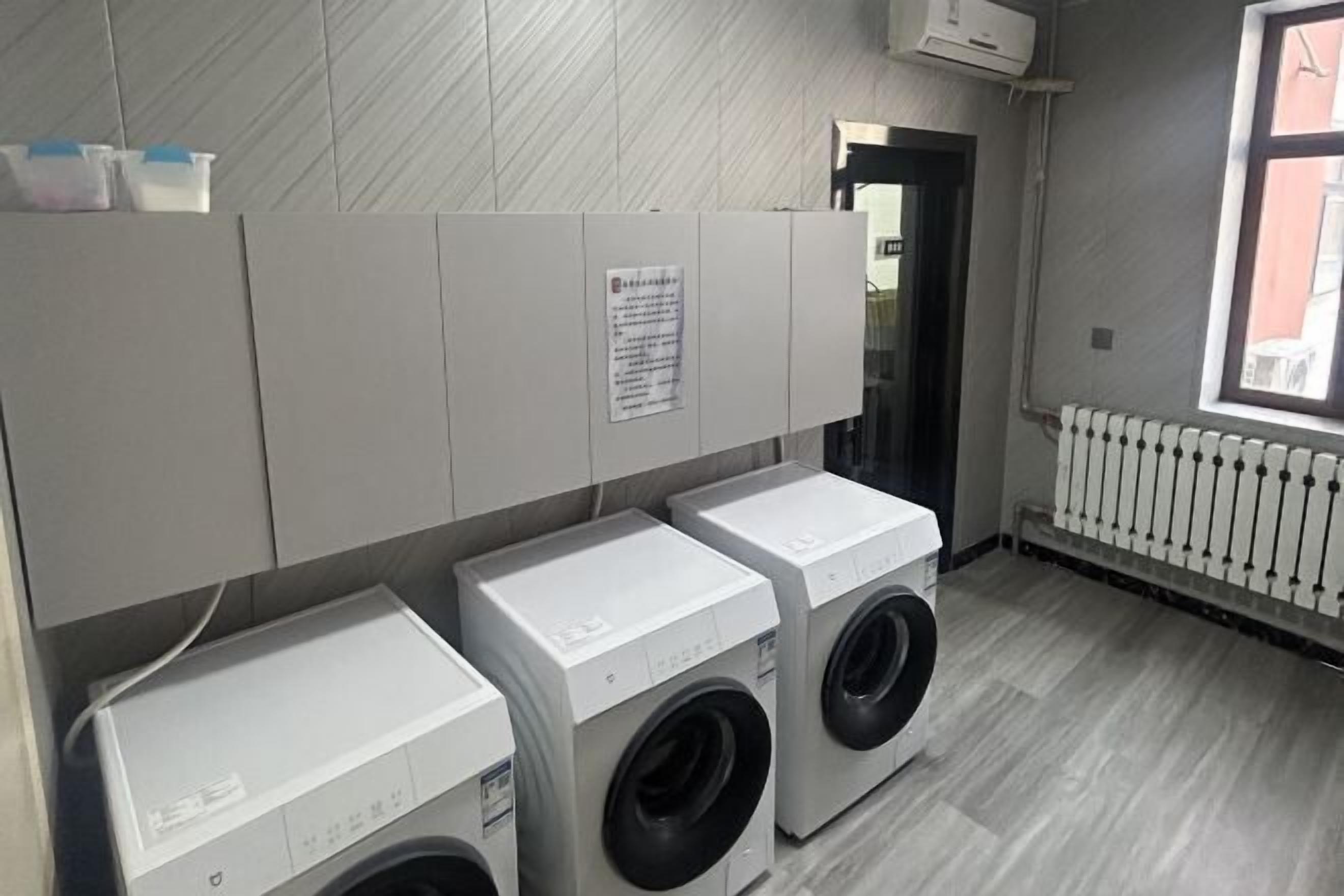 A laundry room with three washing machines and a sign on the wall.
