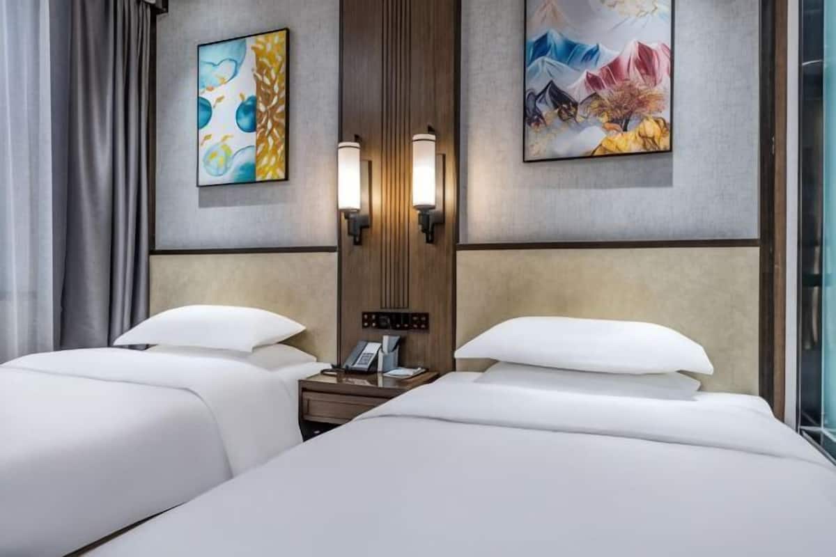 Een hotelkamer met twee bedden, een nachtkastje, wandlampen en kunstwerken.
