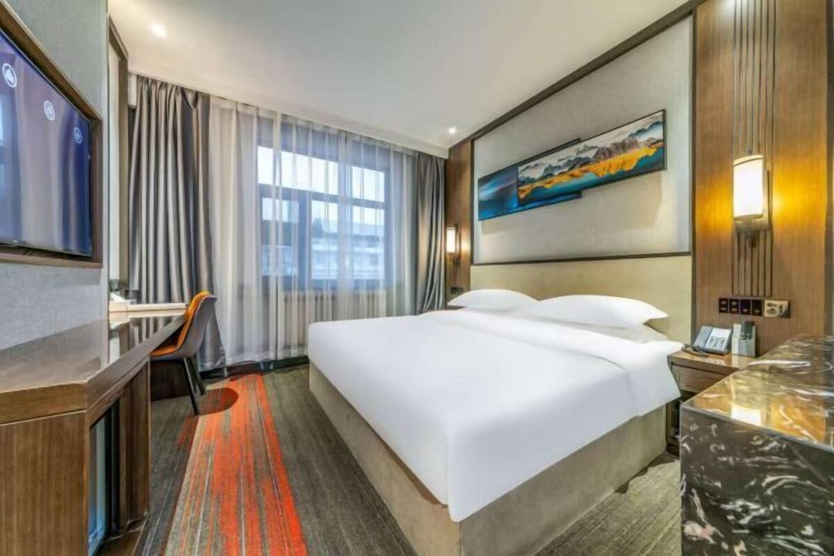 Hotelkamer met een bed, bureau, stoel, televisie, schilderij en een marmeren aanrechtblad.