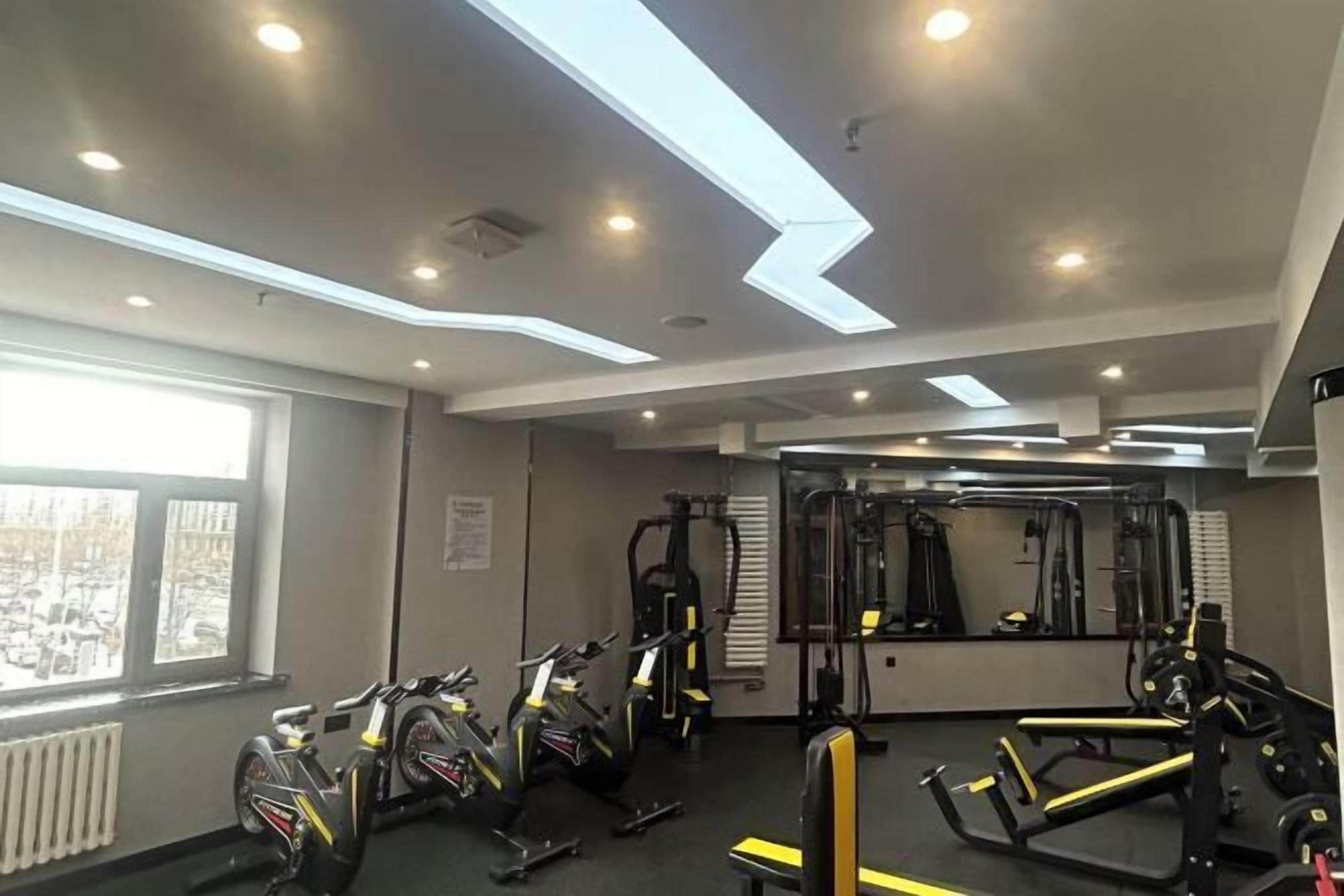 A gym with exercise equipment, a large mirror, and a window with a view of parked cars.