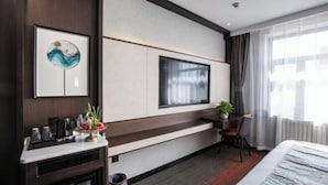 Una habitación de hotel moderna con una cama grande, un televisor montado en la pared, un escritorio con una silla y una pequeña mesa con una planta.