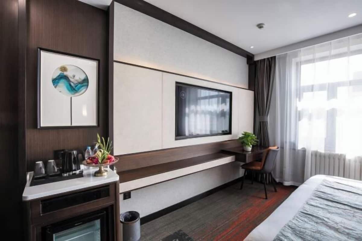 Een moderne hotelkamer met een groot bed, een aan de muur bevestigde televisie, een bureau met stoel en een kleine tafel met een plant.