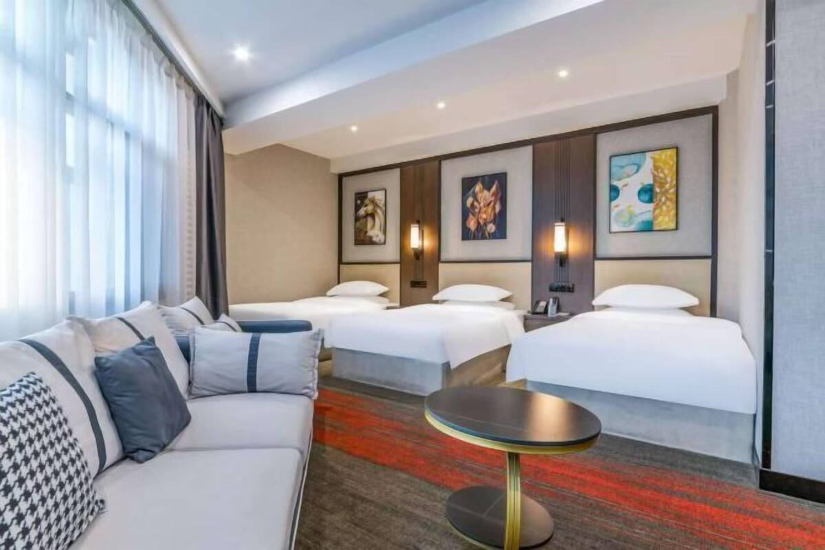 Een hotelkamer met een bank, twee bedden, een ronde tafel en kunstwerken aan de muren.