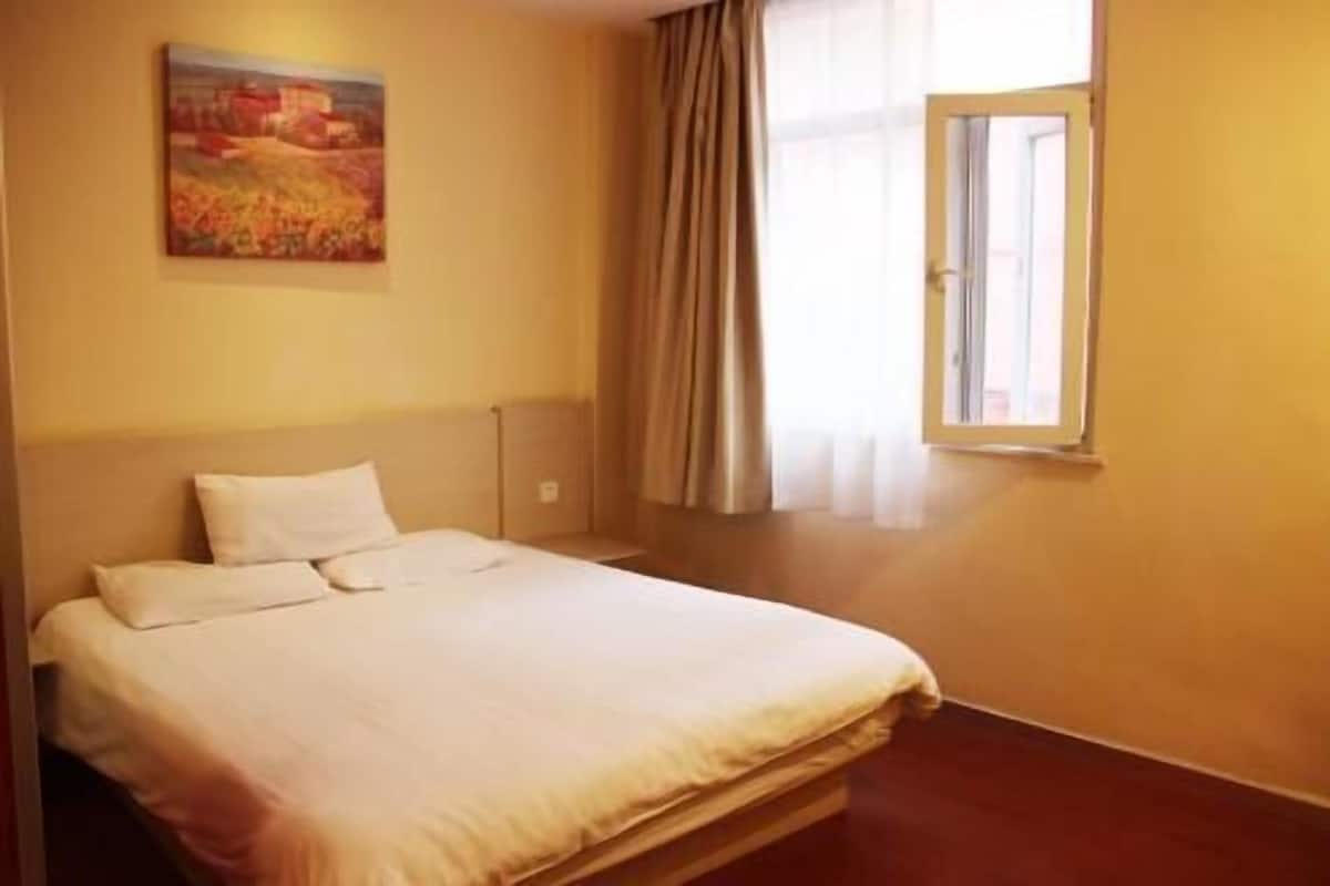 Una camera d'albergo con un letto, un quadro appeso al muro, una finestra con tende e un pavimento in legno.
