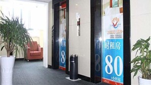 Un'hall dell'hotel con una reception, un divano rosso, piante in vaso e un grande poster promozionale.