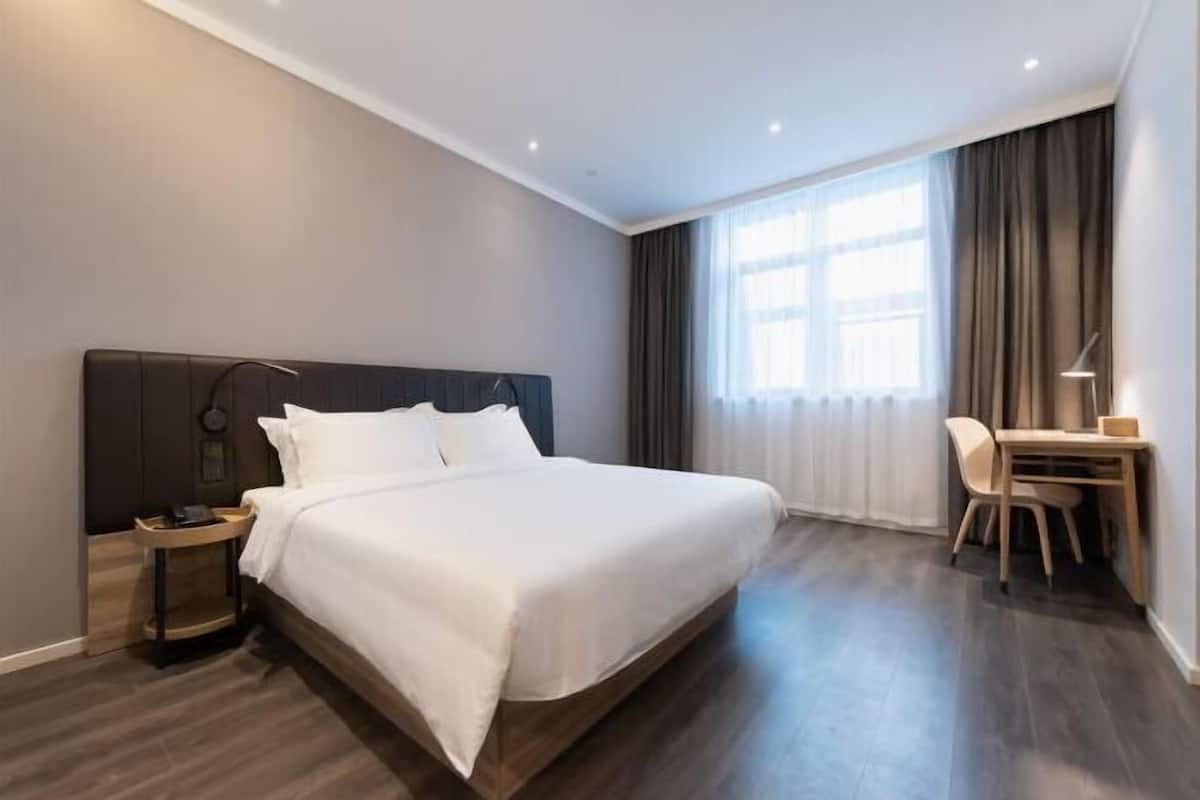 Una camera d'albergo con un letto grande, una scrivania con una sedia e una finestra con tende.