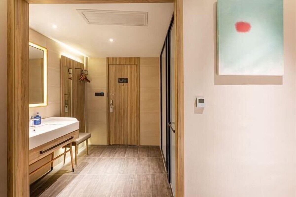 A hallway with a wooden door, a bench, a mirror, and a wall-mounted artwork.