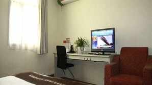 Una camera d'albergo con un letto, una scrivania con un computer, una sedia, una pianta in vaso e un condizionatore d'aria.