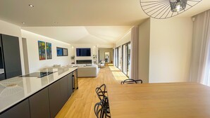 Una cocina moderna con una isla central, un comedor con mesa y sillas de madera, y una sala de estar con sofá y televisor.