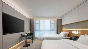 Habitación de hotel con televisión de pantalla plana, dos camas, una mesita con un florero y un ventanal con cortinas.