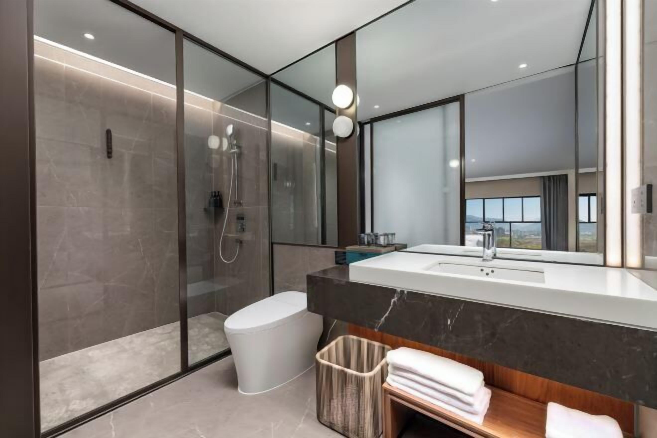 A modern bathroom with a glass-enclosed shower, a white toilet, a large mirror, and a marble countertop.
