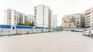 Un estacionamiento con varios coches, una barrera azul y edificios al fondo.